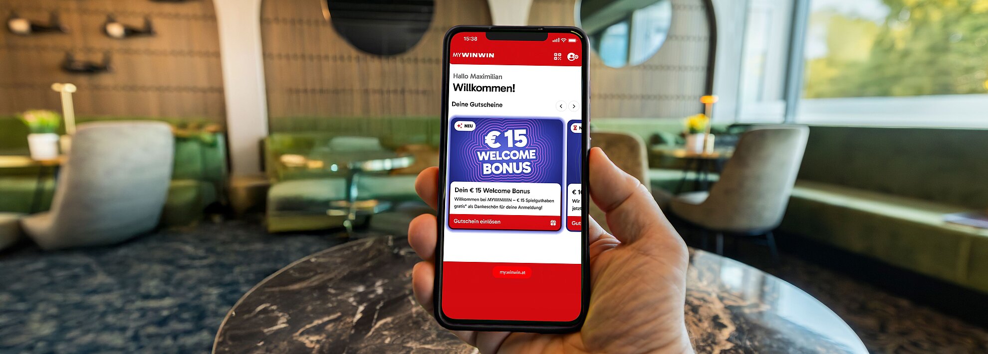 Es ist ein Handy zu sehen, auf dem der Welcome Bonus in der MYWINWIN Applikation gezeigt wird. 